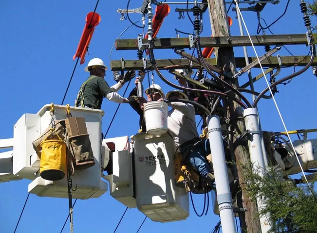 Two Plant Wide Services linemen working from a bucket truck on a utility pole in clear daylight.